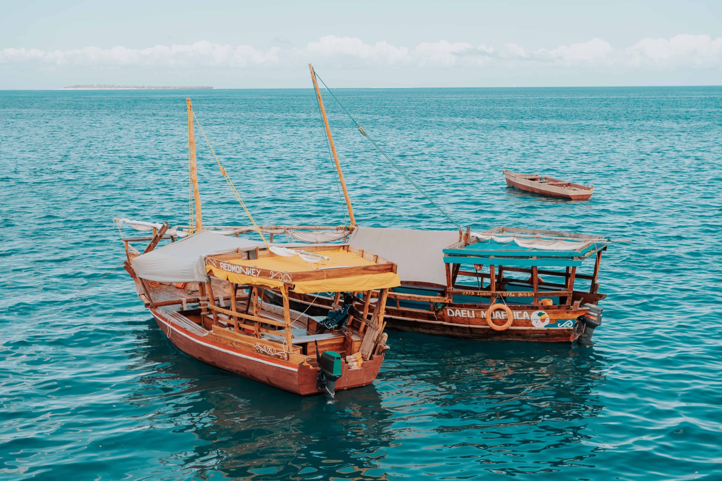 Two wooden dhows with canopies moored on turquoise water off Zanzibar.
